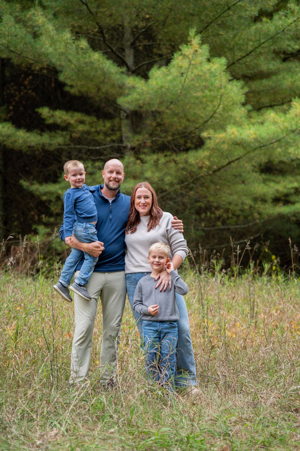A group poses together in a sunny field with evergreen trees in the background.