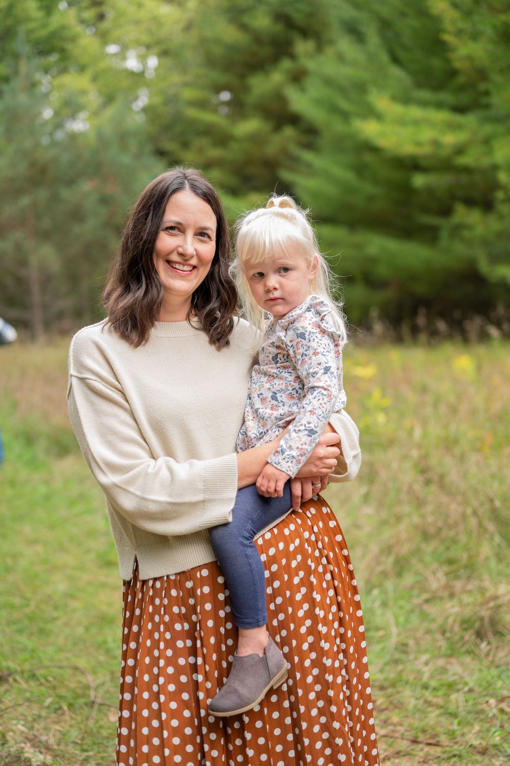 Two people in matching brown polka dot skirts stand together in a grassy outdoor setting.