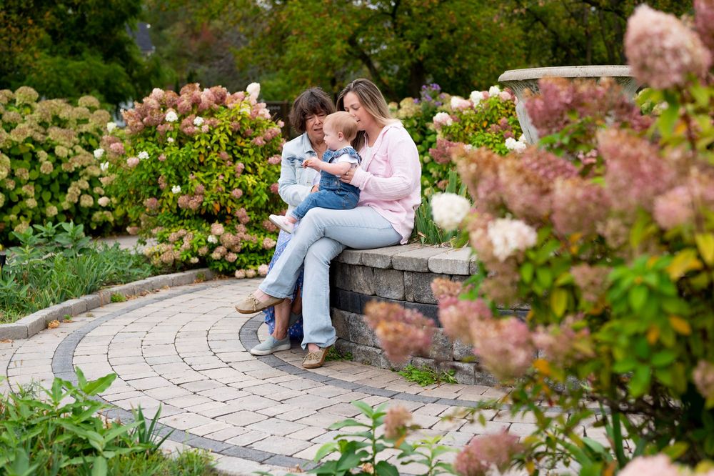 A curved stone garden wall with pink flowering bushes creates a peaceful seating area in a lush outdoor setting.