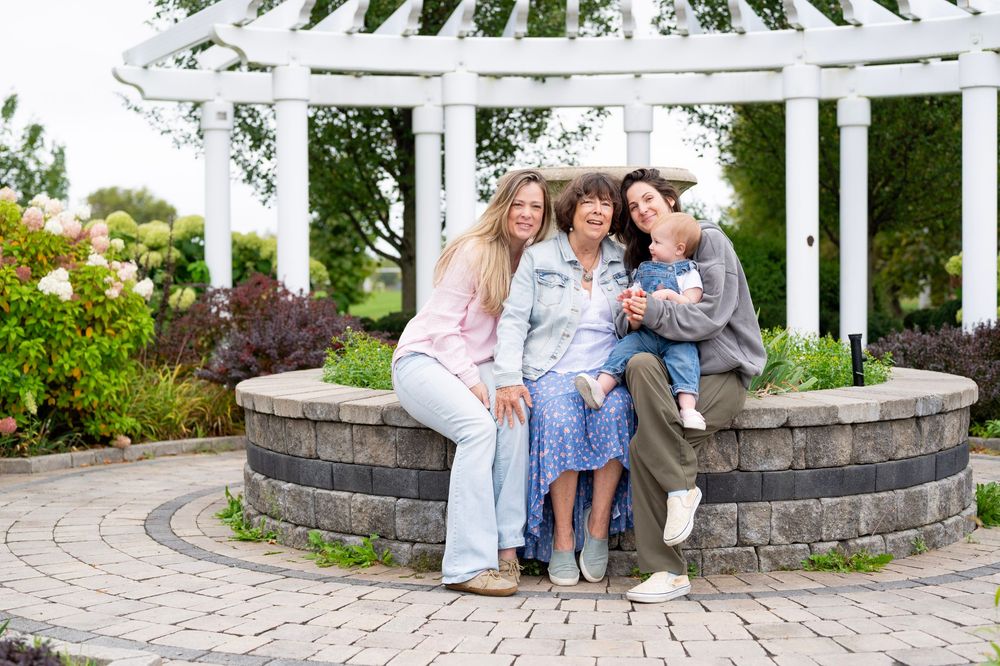 A white garden pergola frames a curved stone wall with pink blooming flowers in a landscaped outdoor space.