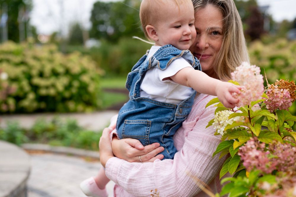 A parent and child share tender moments outdoors among blooming flowers and greenery on a sunny spring day.