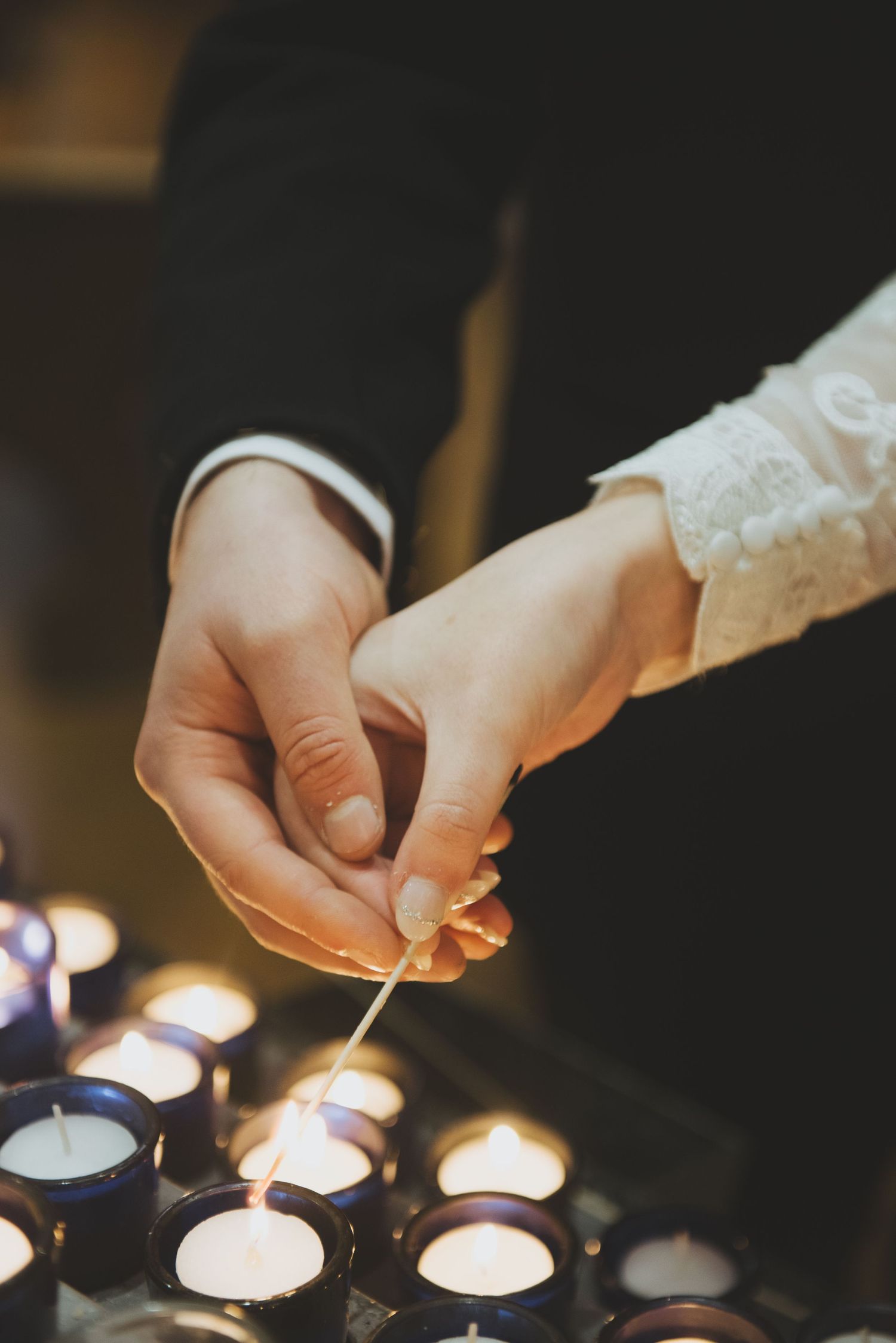 Bride and groom lighting small tea light prayer candles in glass holders creating an intimate atmosphere with soft glowing flames.