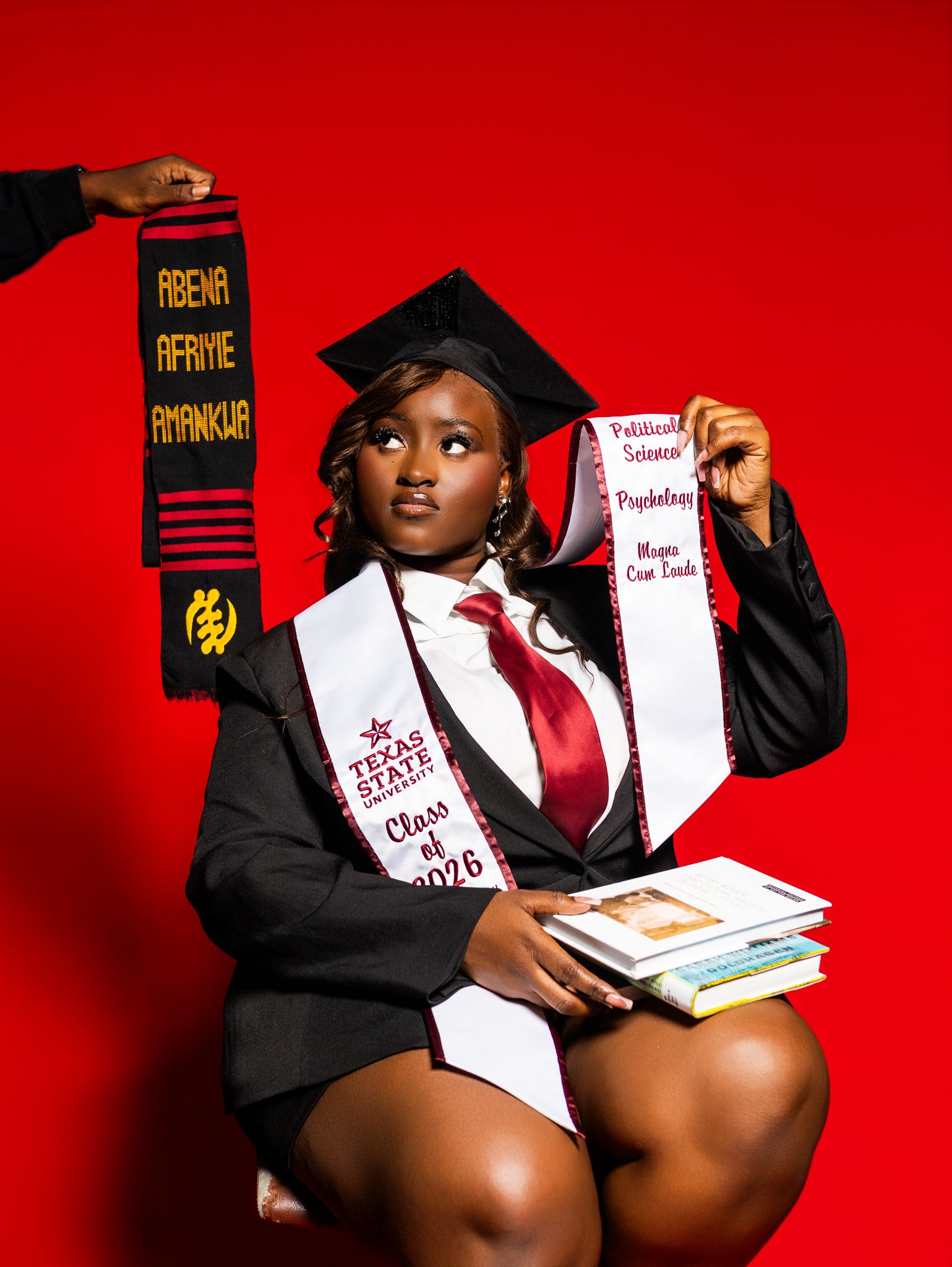 Texas State University graduate poses in cap and gown holding kente stole and diploma, Class of 2026.