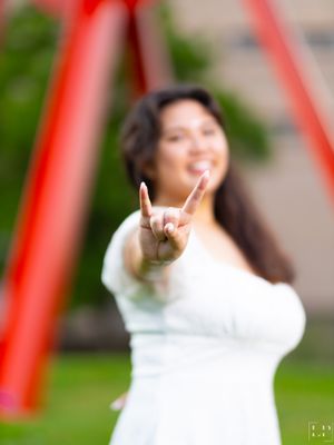 Person in white outfit making rock and roll hand gestures against red background.