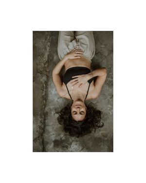 Artistic overhead portrait of someone with dark curly hair laying on textured concrete in moody lighting.