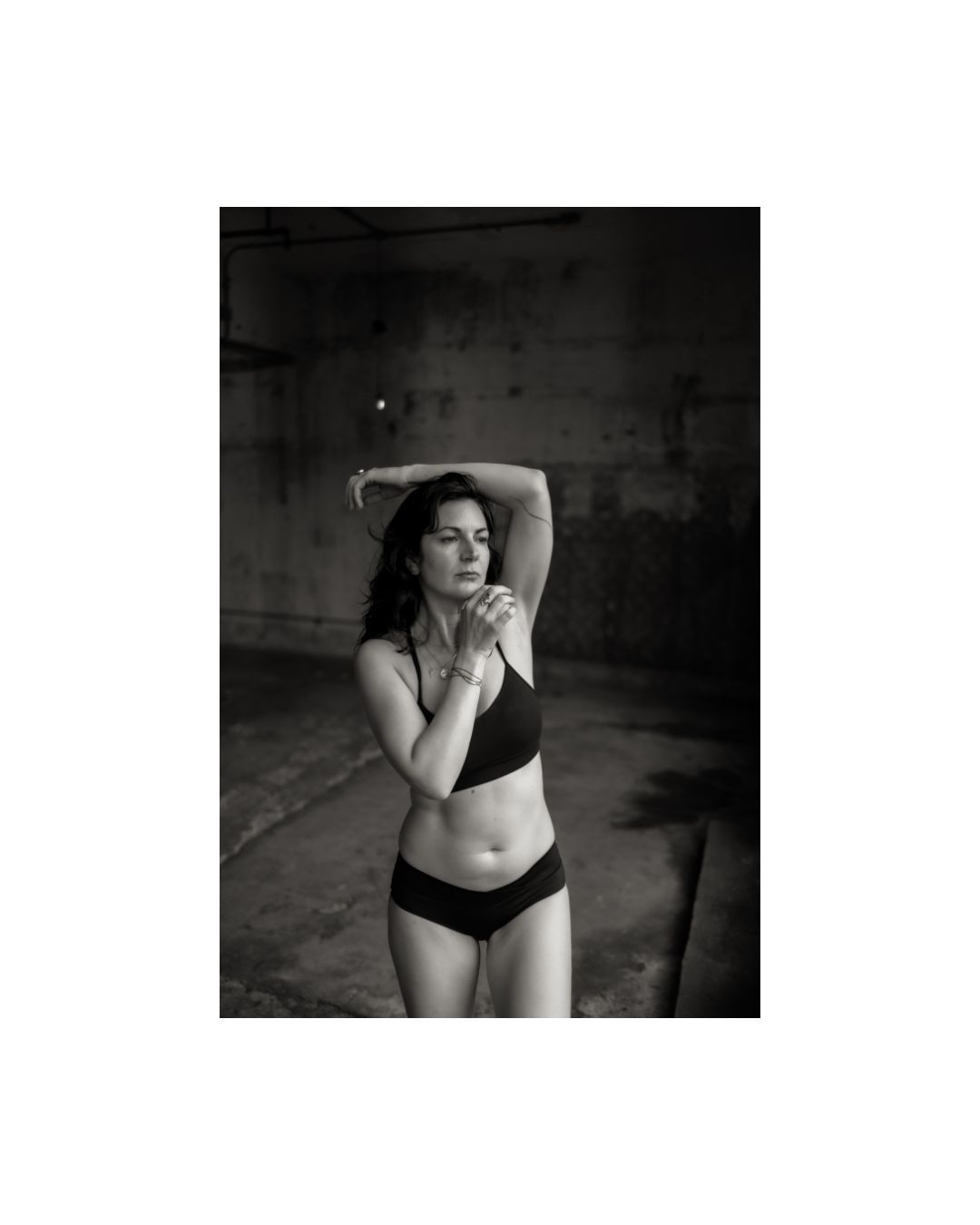 Black and white artistic photos show a person in dark intimate apparel against a moody, shadowy background.