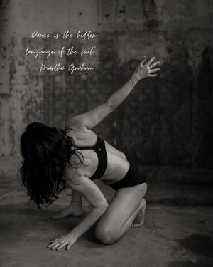 Black and white artistic dance photo showing a dancer in athletic wear posing expressively against a textured wall.