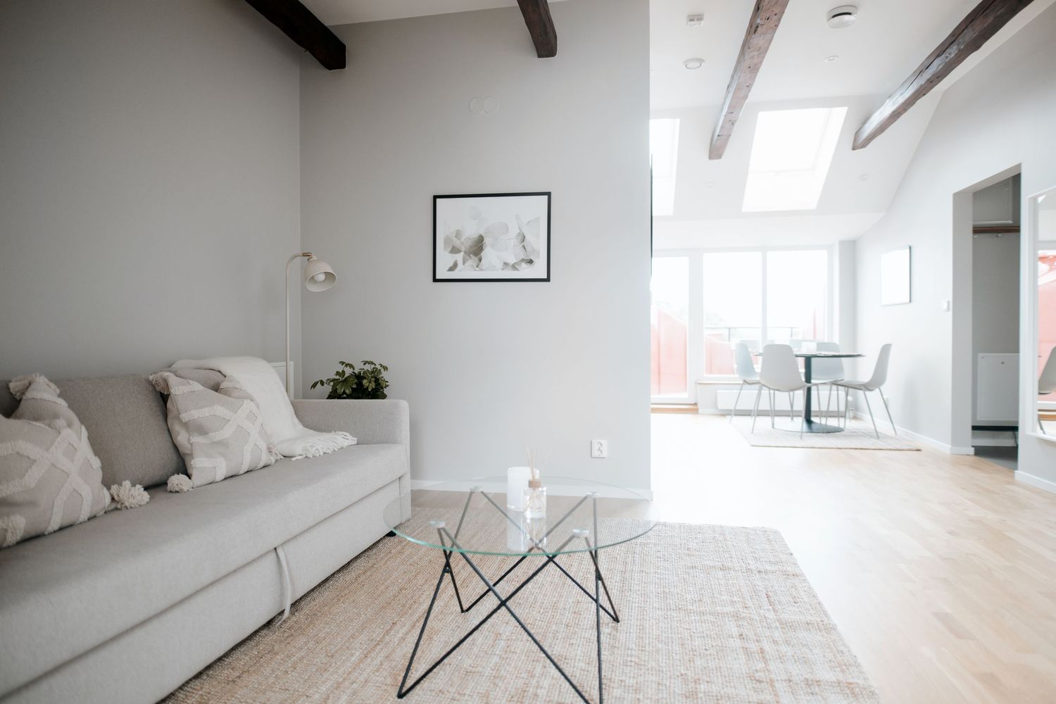 Modernt minimalistiskt vardagsrum med grå soffa, glasbord och takbjälkar i trä. Vasastaden, Stockholm