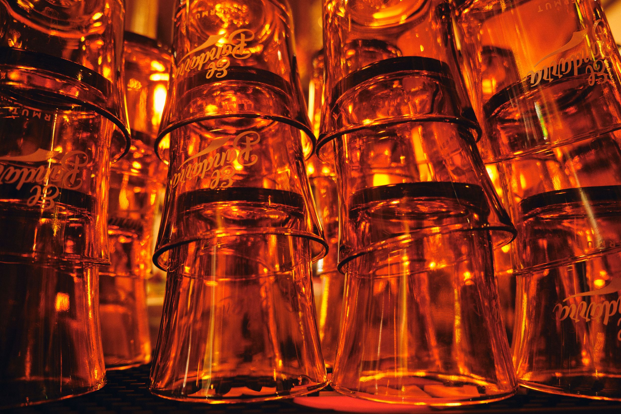 Glowing amber glass tumblers stacked in rows creating a warm illuminated pattern.