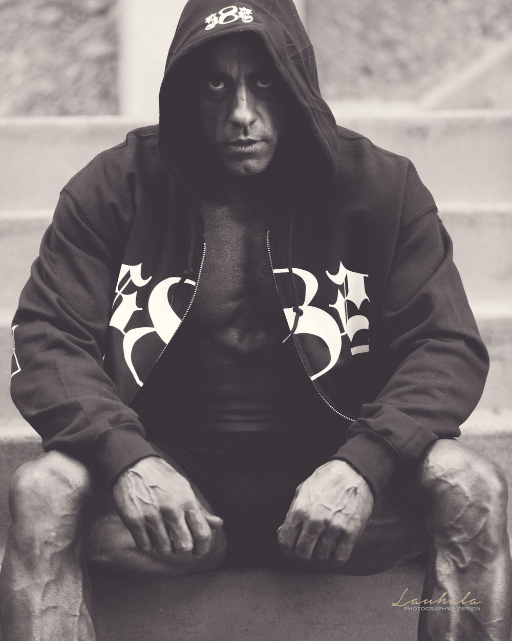 Moody black and white portrait of person in hooded sweatshirt sitting on steps.
