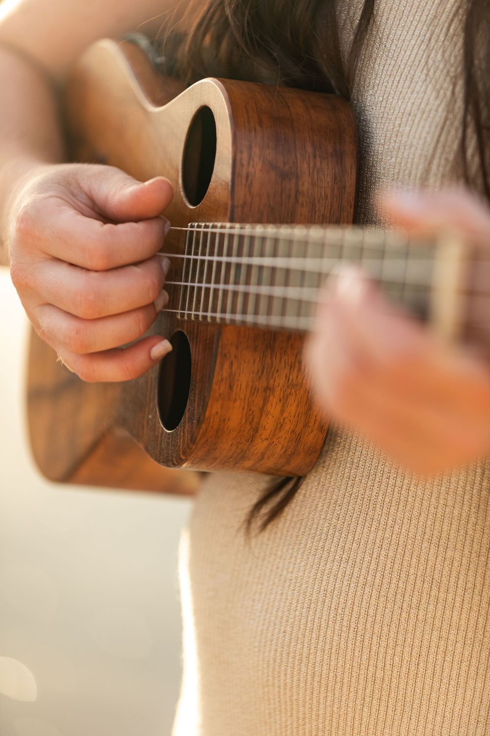 Close-up of hands playing wooden ukulele with soft natural lighting.