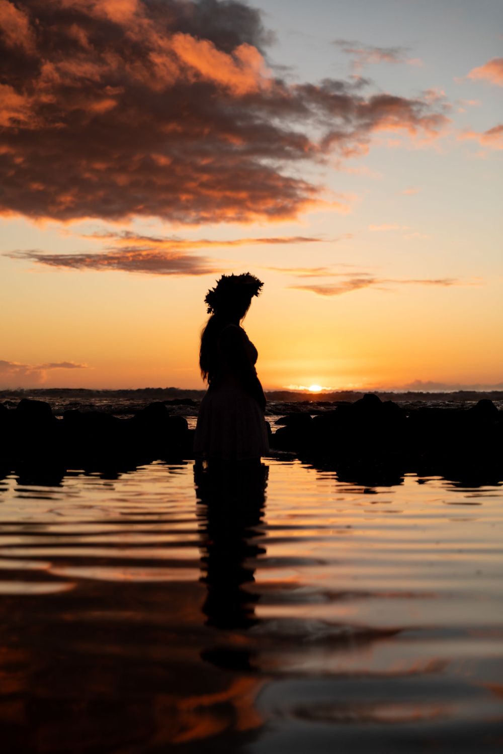 Silhouette figure in water against dramatic orange sunset sky.