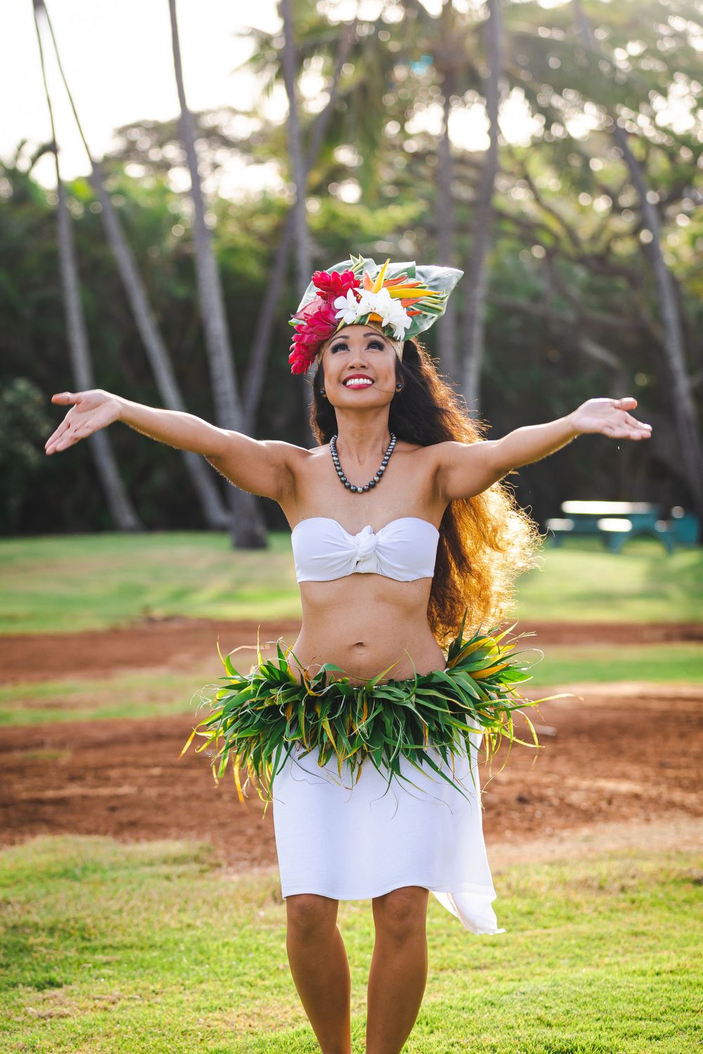Traditional Hawaiian dancer performs in grass skirt and floral lei among palm trees.
