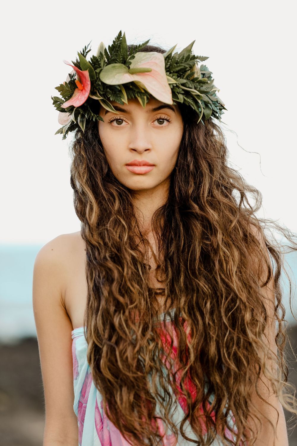 Portrait of a model wearing a tropical flower crown and floral dress on a Hawaiian beach.