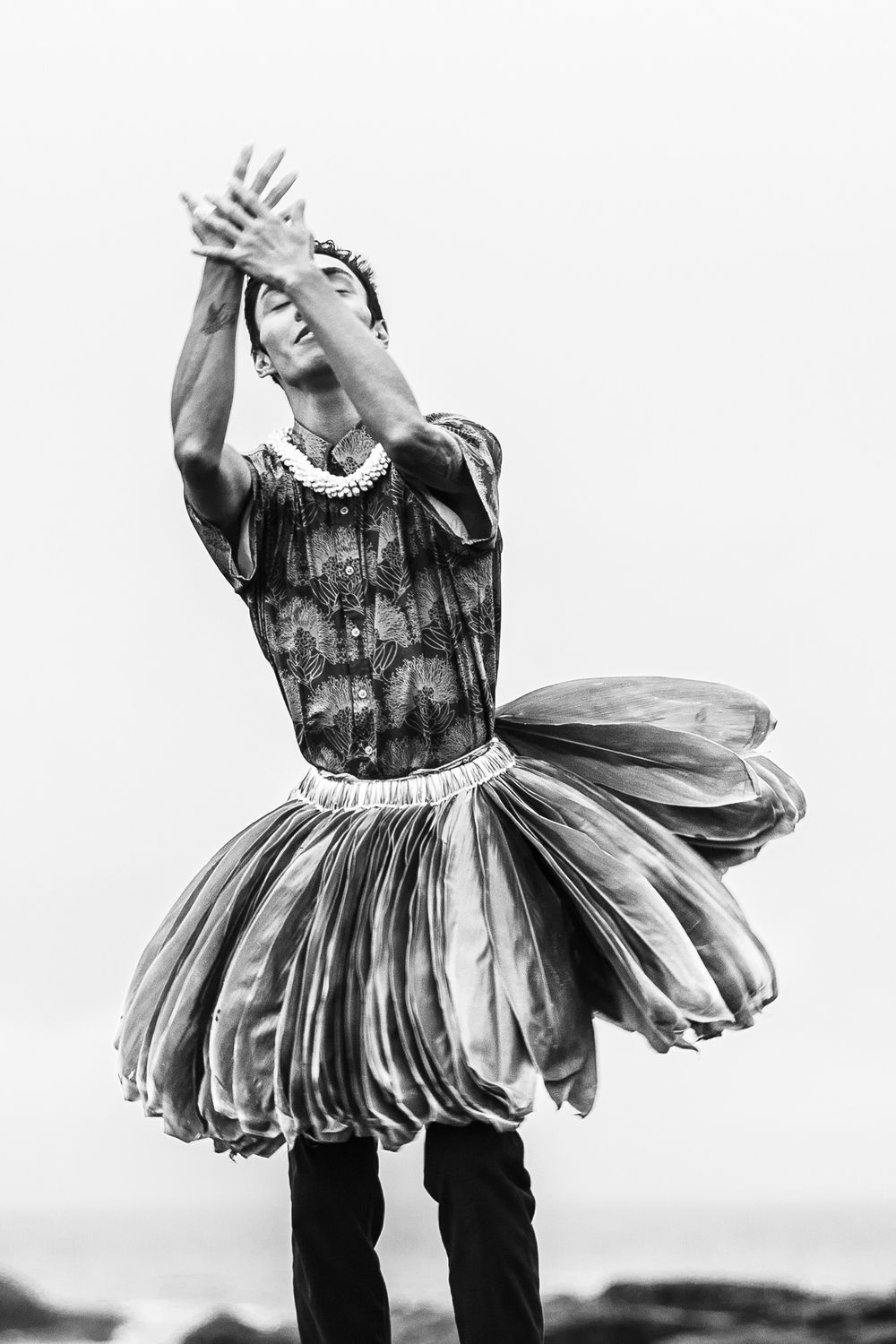 A dramatic black and white portrait of a dancer in a floral tutu with raised arms.