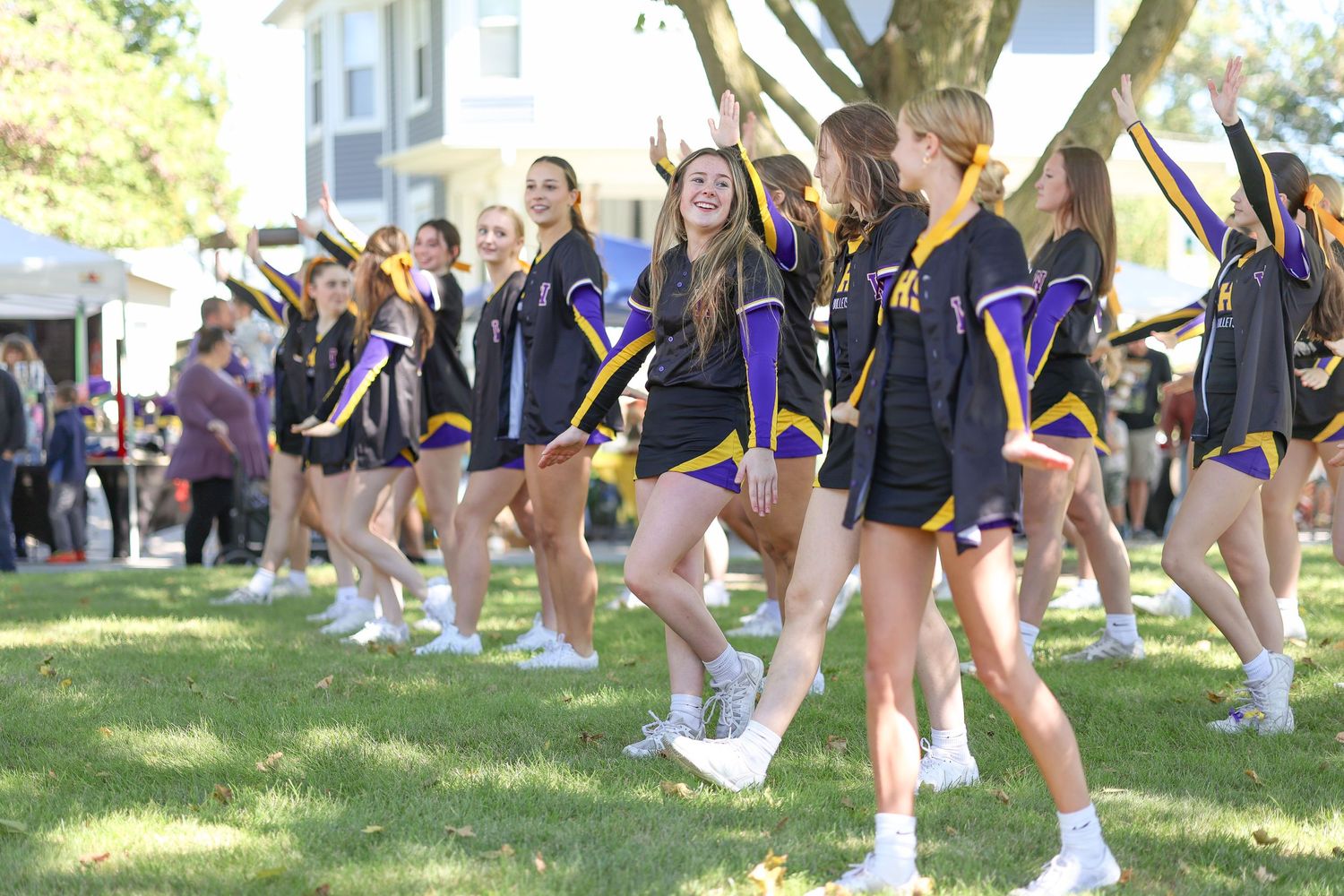 Cheerleaders in purple and black uniforms perform a routine on a sunny grass field.