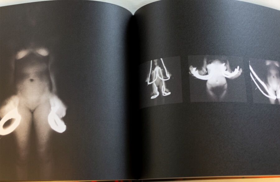 Dark photography book spread showing ethereal ghostly figures in white against black background.