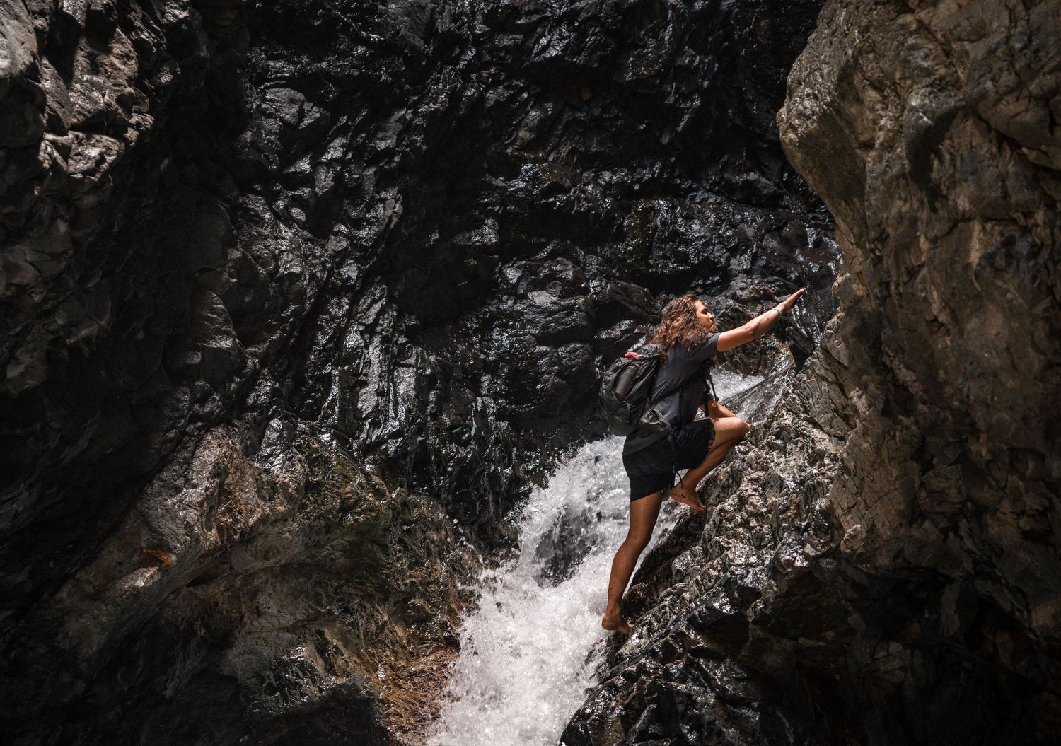 A rock climber scales a wet cliff face near a cascading waterfall.
