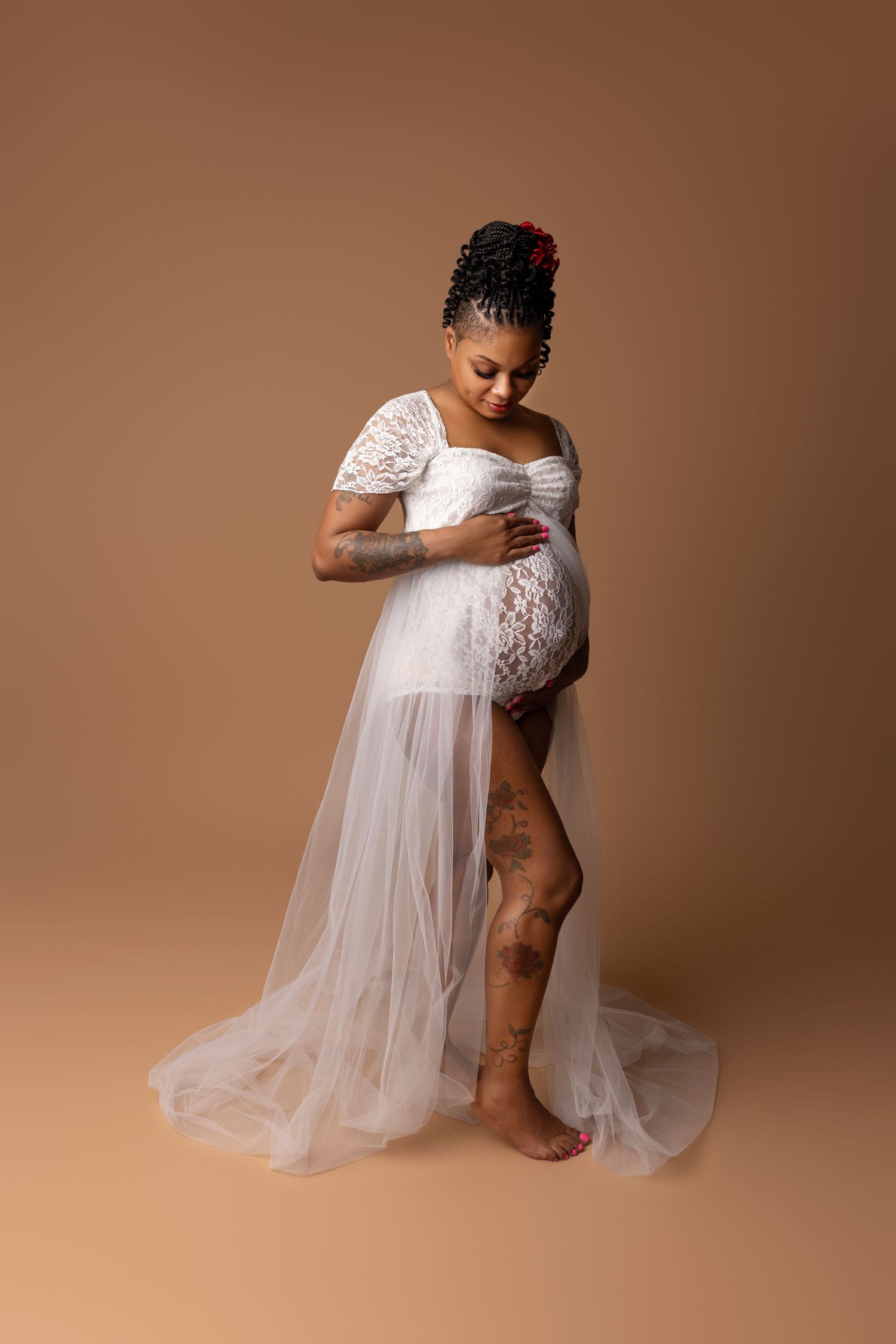 Expecting mother in a white tulle and lace dress, showcasing her baby bump in a pregnancy photo studio in