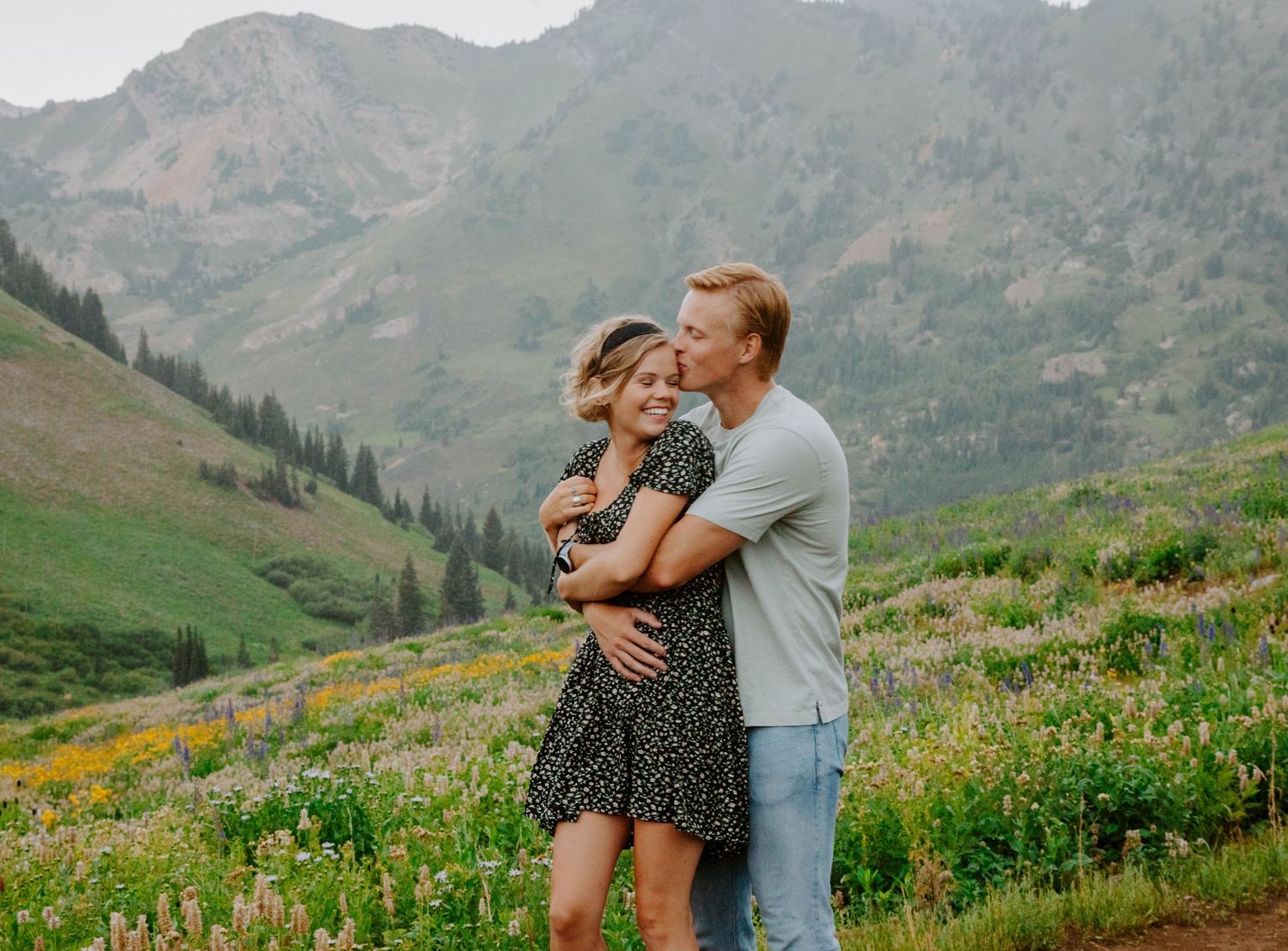 Couple shares intimate moment in mountain meadow surrounded by wildflowers.