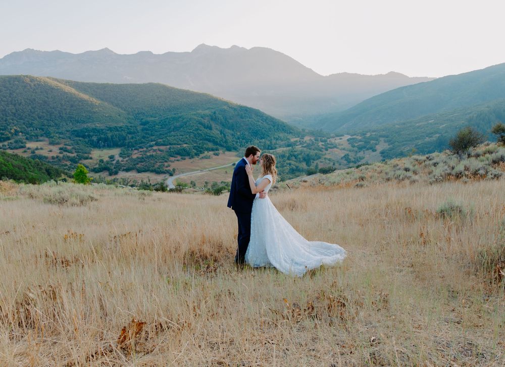 Bride and groom embracing in golden field with stunning mountain valley backdrop on their wedding day.