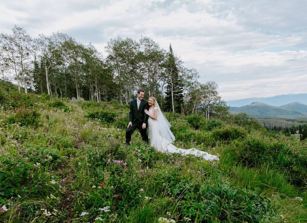 Bride and groom stand on a lush green mountain hillside with sweeping valley views on their wedding day.