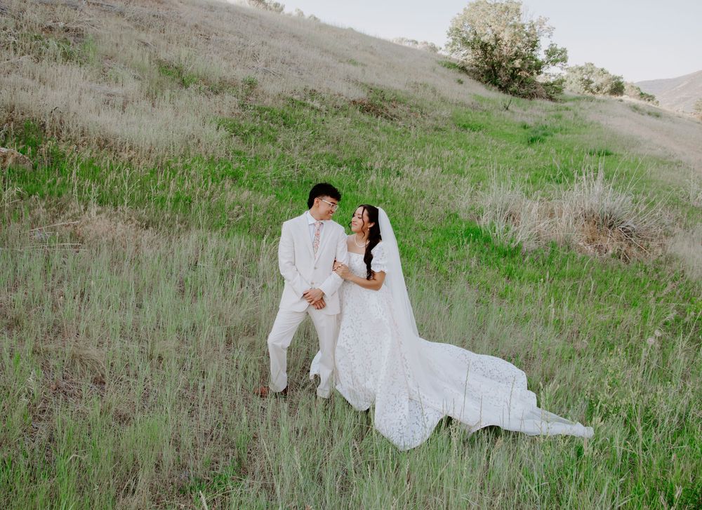 Bride and groom holding hands on a lush green hillside, bride in a flowing white gown with veil.