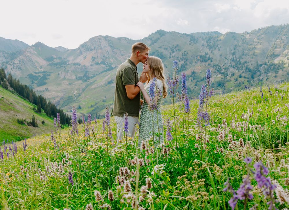 Couple sharing a romantic moment in a wildflower meadow with purple lupines and mountain backdrop.