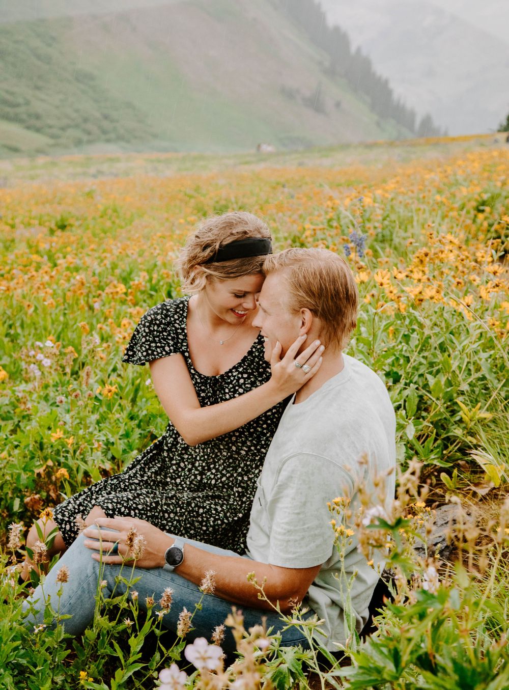 A couple shares an intimate moment in a wildflower meadow with mountain views.