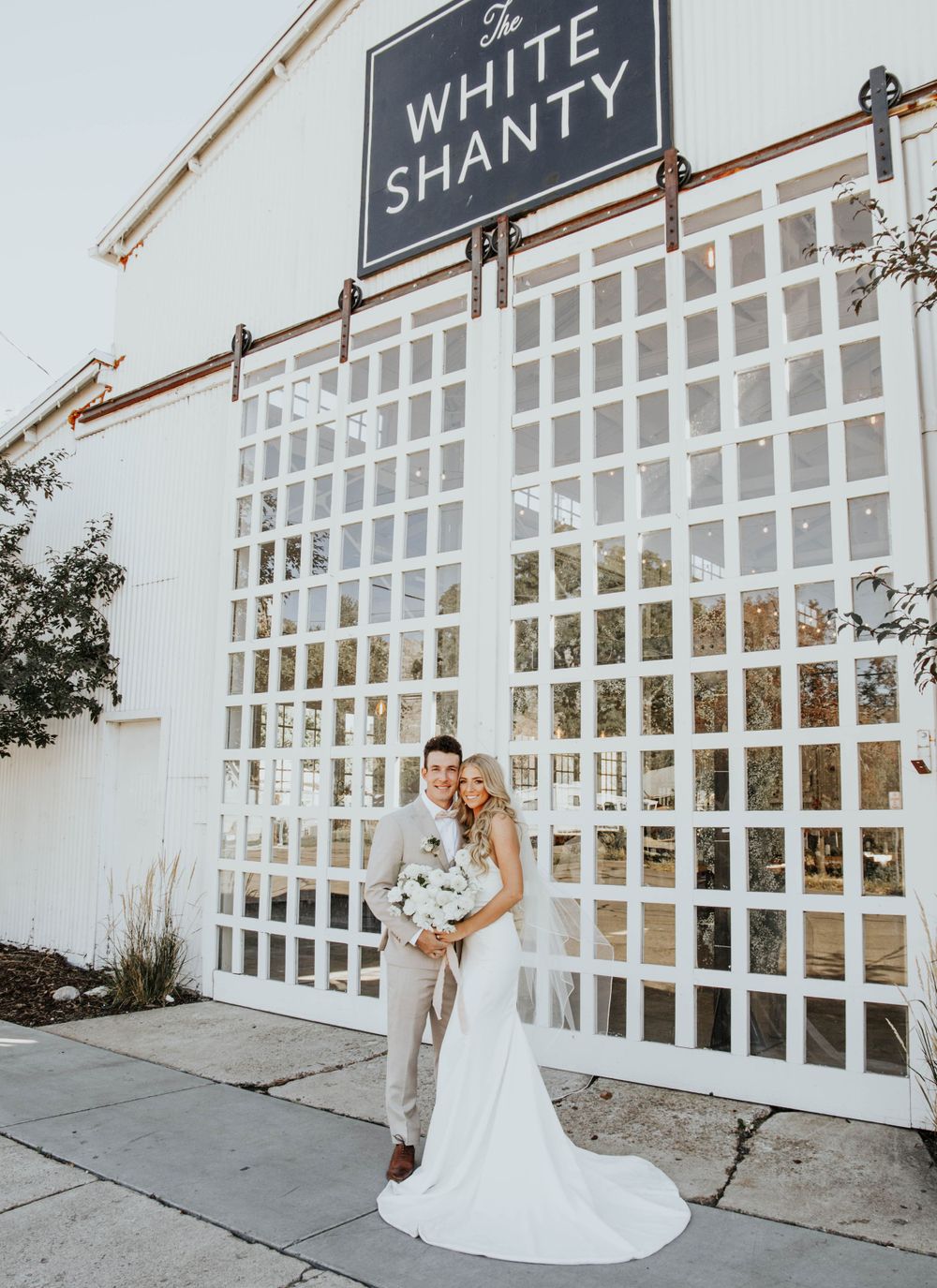 A wedding portrait in front of The White Shanty venue featuring modern lattice architecture.