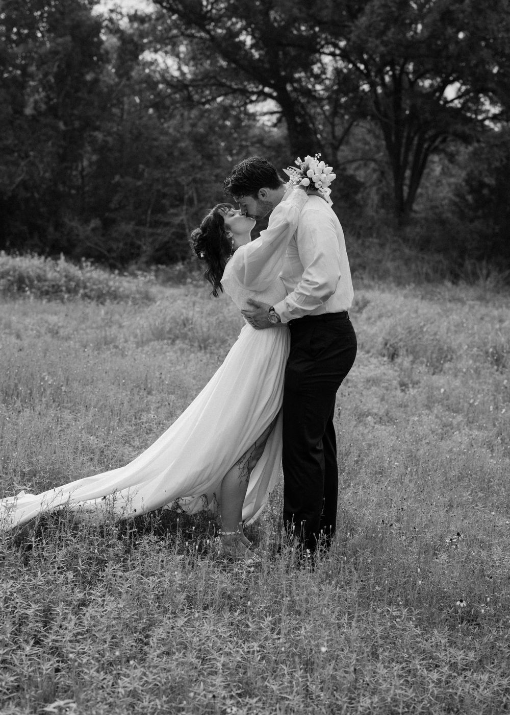 A romantic black and white photo of a couple embracing in a meadow.
