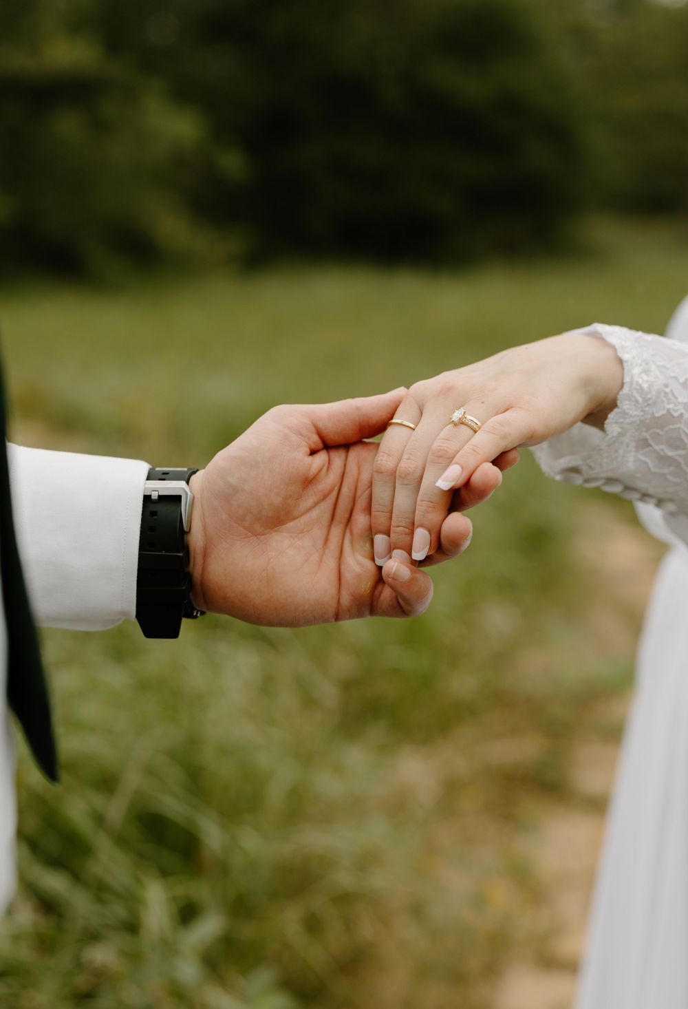 Close-up shot of hands clasped together showing wedding rings against white clothing.