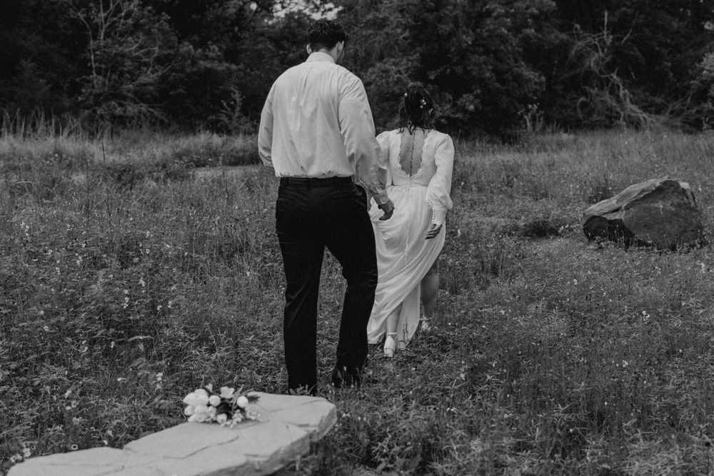A couple walks through a wildflower field in wedding attire.
