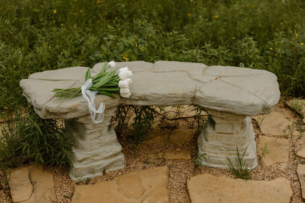 White flowers rest on a rustic stone bench in an outdoor garden setting.
