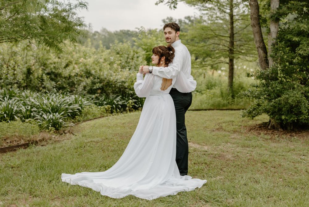A couple embraces in a romantic garden setting with the bride wearing a flowing white gown with a long train.