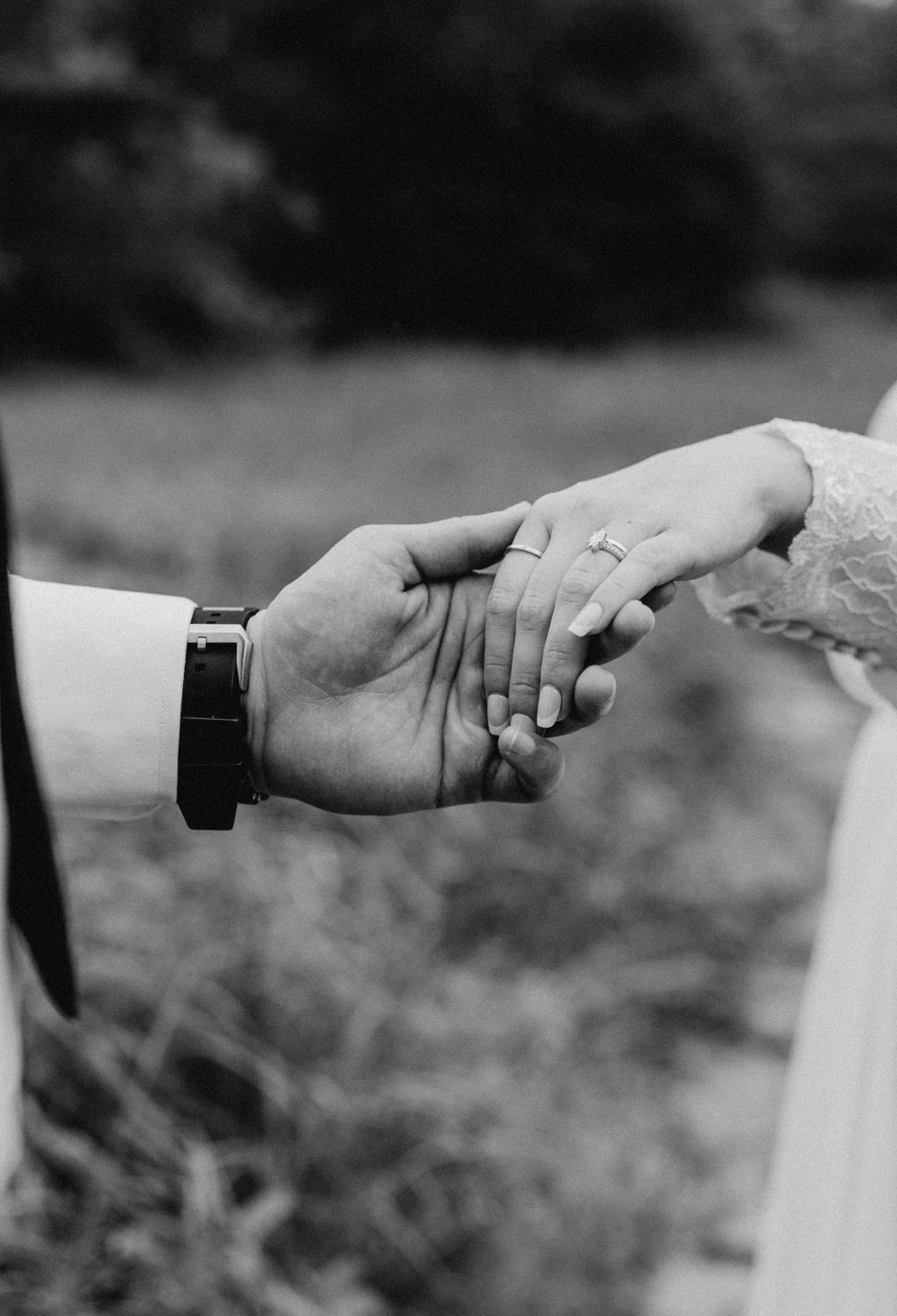 A close-up black and white photo of hands with wedding rings.