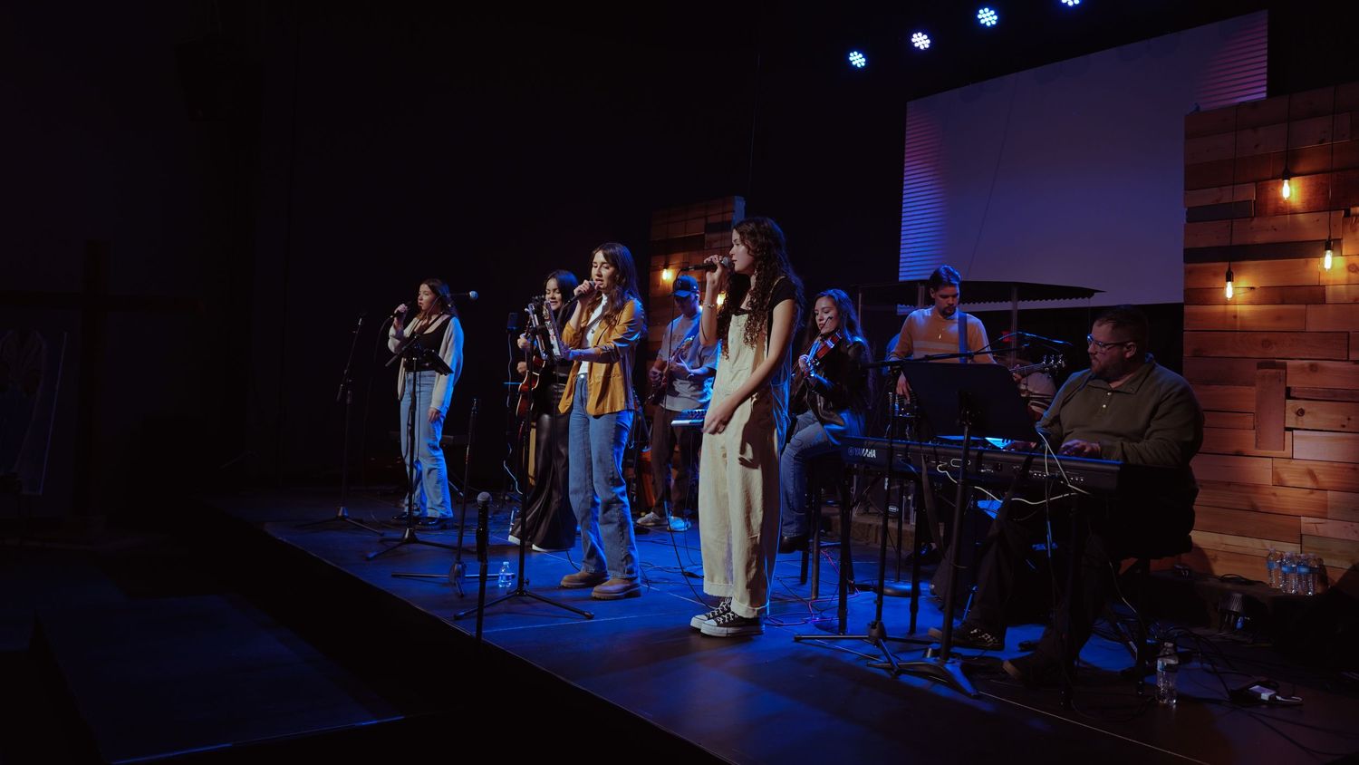 Musicians performing on stage with instruments under blue stage lighting.