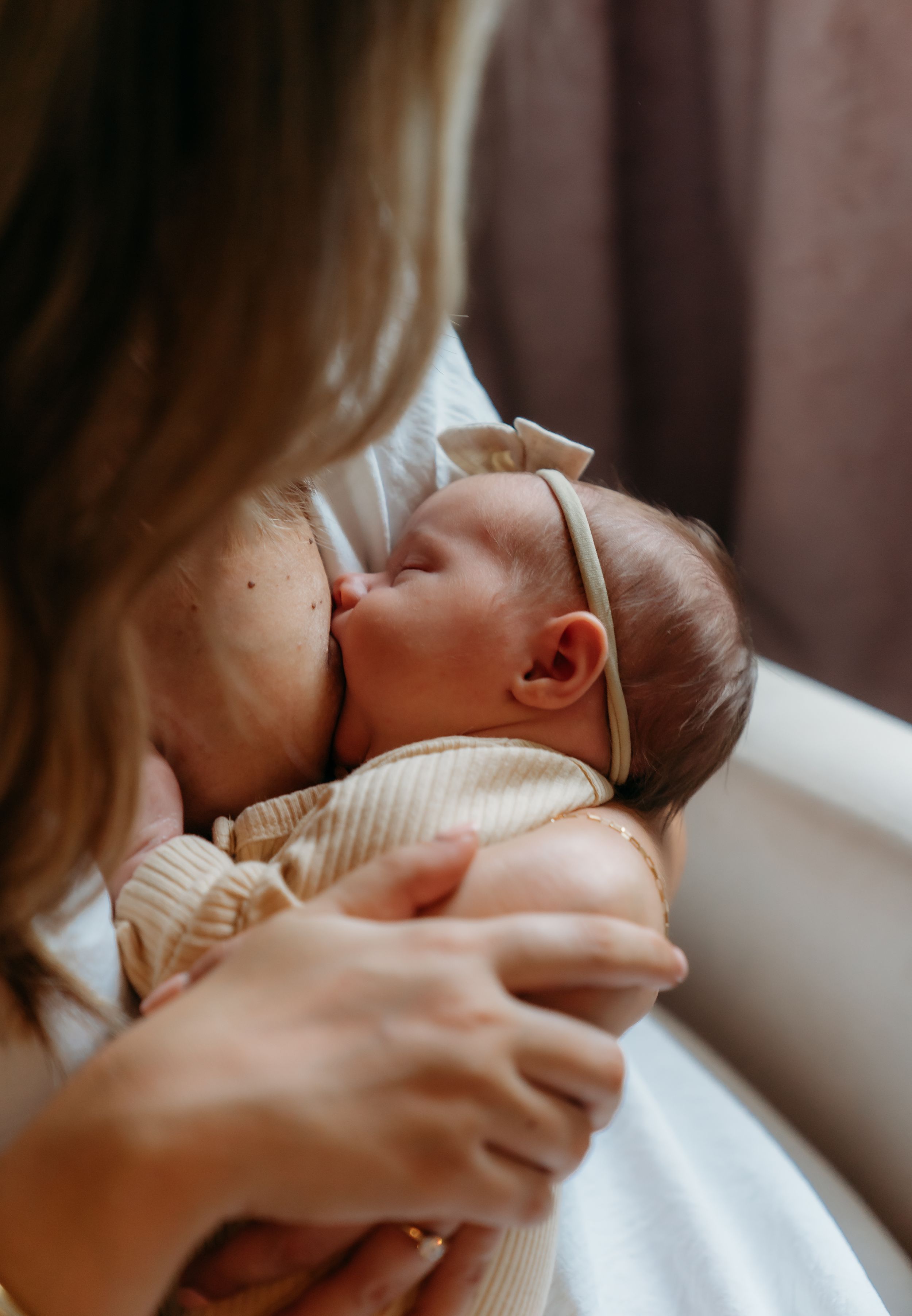 Tender moment with sleeping newborn in striped onesie against soft lighting.