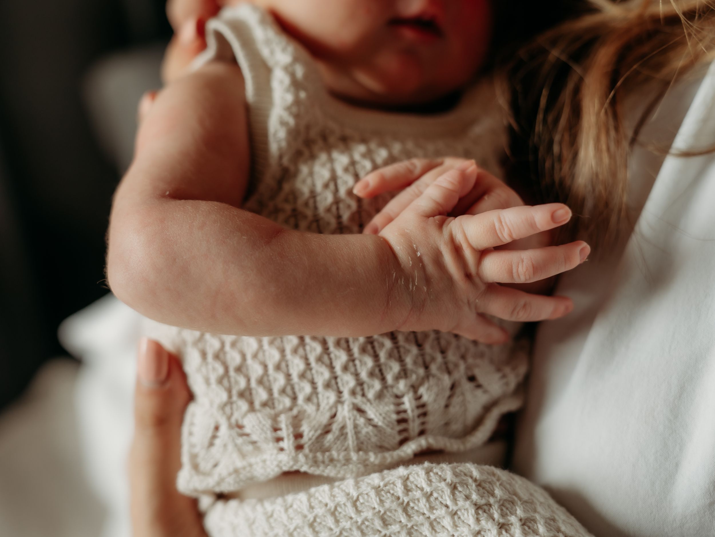 Close-up of tiny baby hands grasping while wearing a knitted white dress.