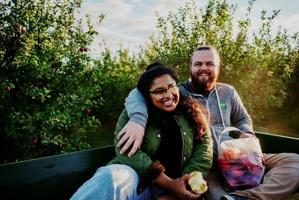 Smiling couple embracing in a wagon surrounded by lush apple trees at an orchard.