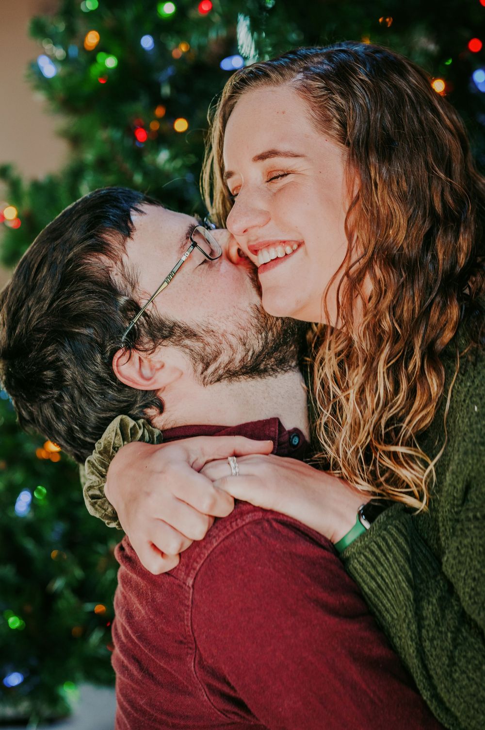 Joyful couple embracing and laughing in front of a decorated Christmas tree.