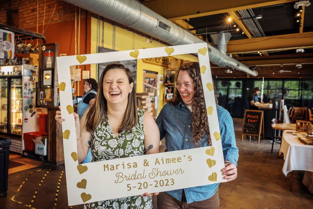 Two women posing with Marisa and Aimee bridal shower decorative frame.