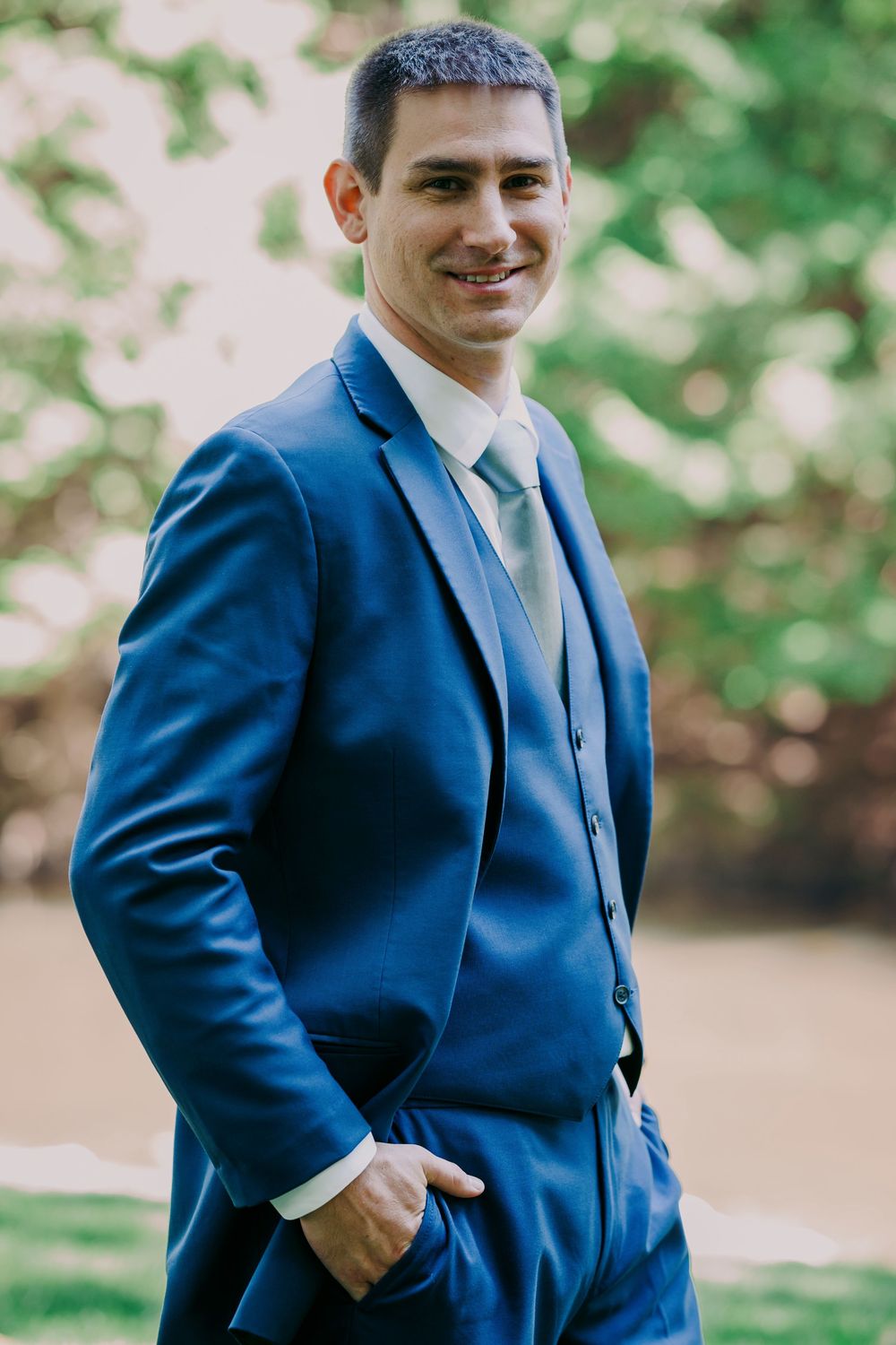 Smiling groom in blue suit posing outdoors.