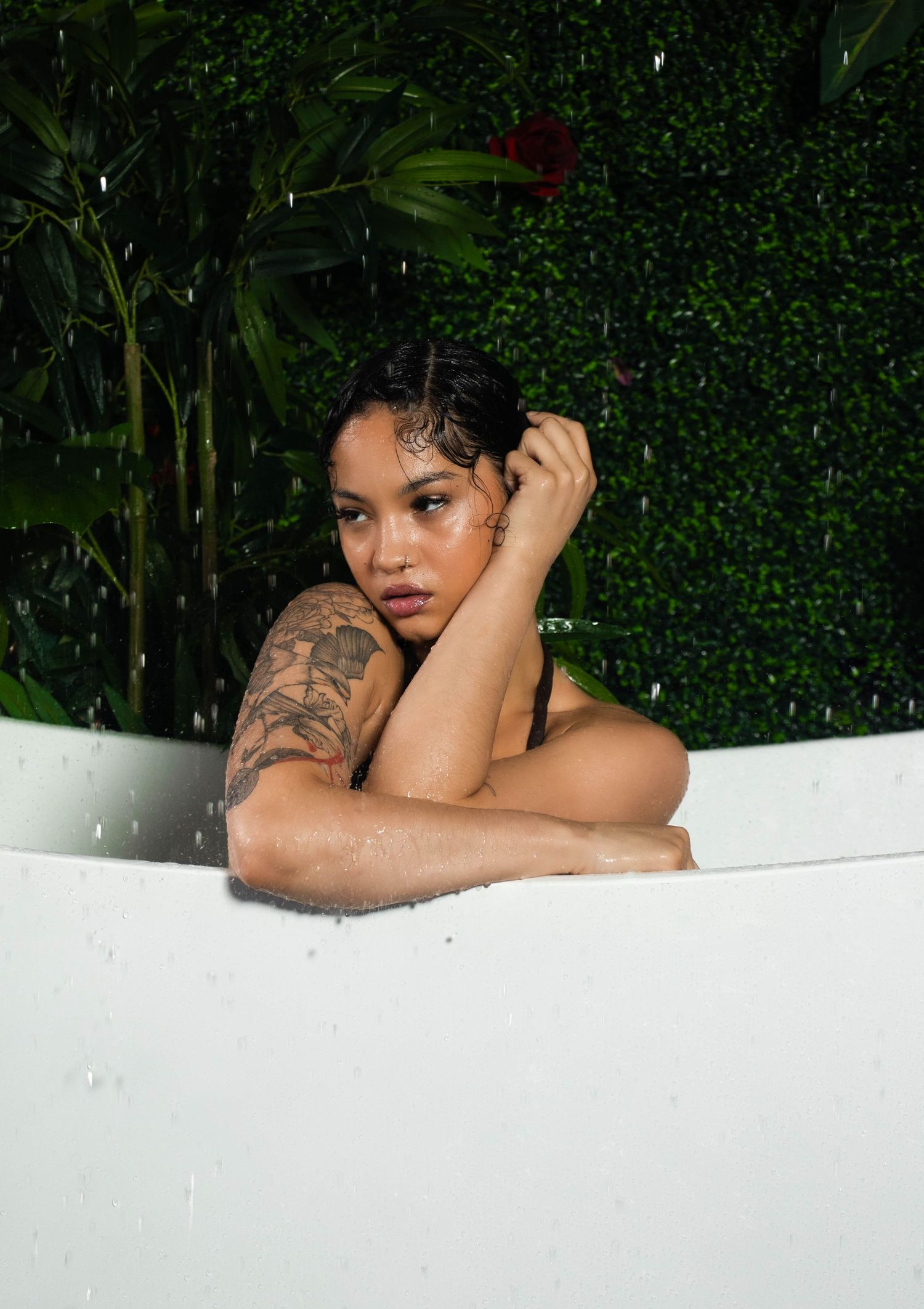 Artistic bathtub portrait with lush green foliage backdrop and white porcelain tub creating a tropical spa-like setting.