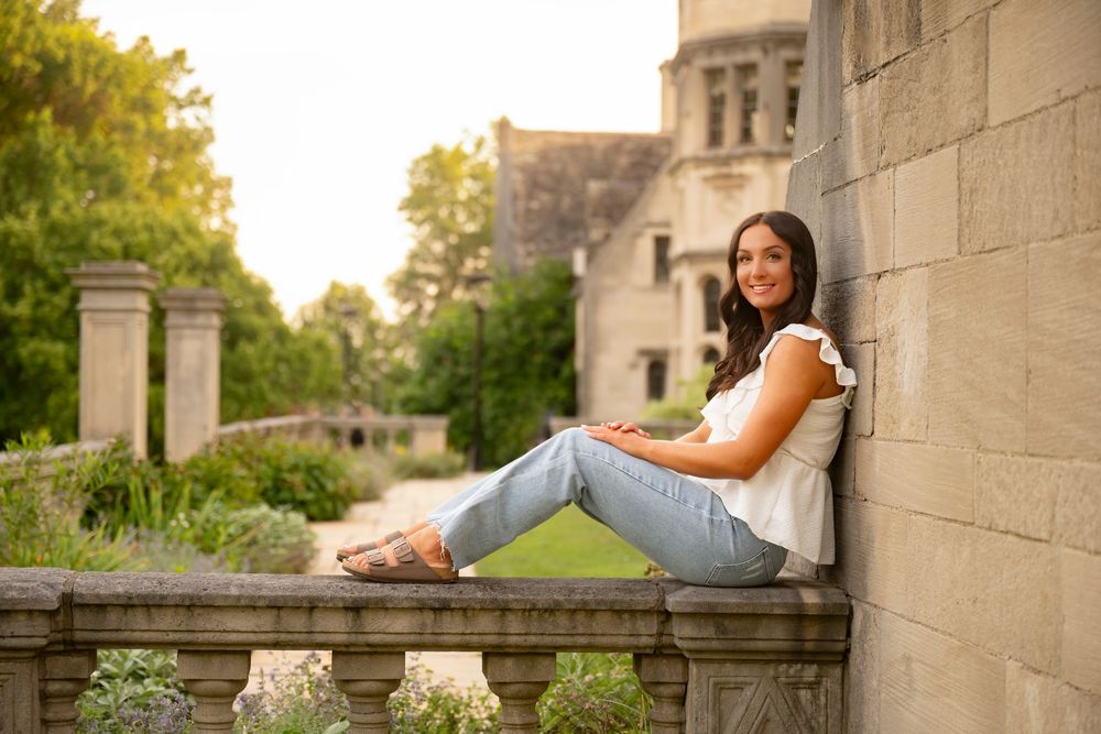 A person in casual attire relaxes on a stone ledge against a wall during a sunny afternoon.