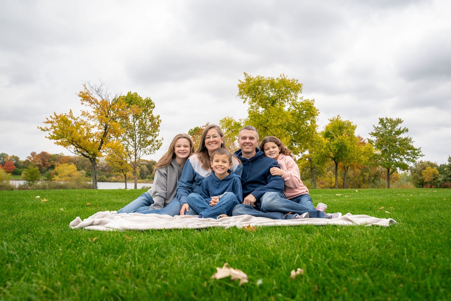 Family group lying on white blanket in green grass field during autumn.