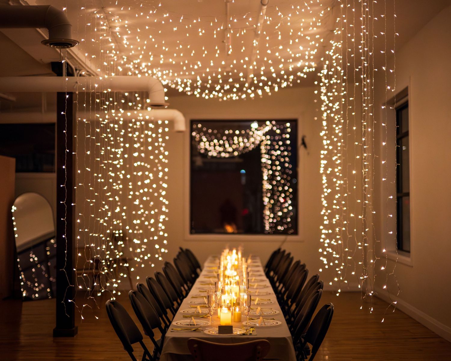 Long dining table illuminated by candles and elegant cascading string lights creating a magical indoor setting.