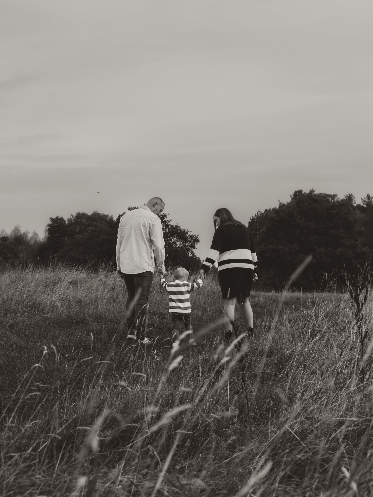 A family walking through tall grass in a field on an overcast day.