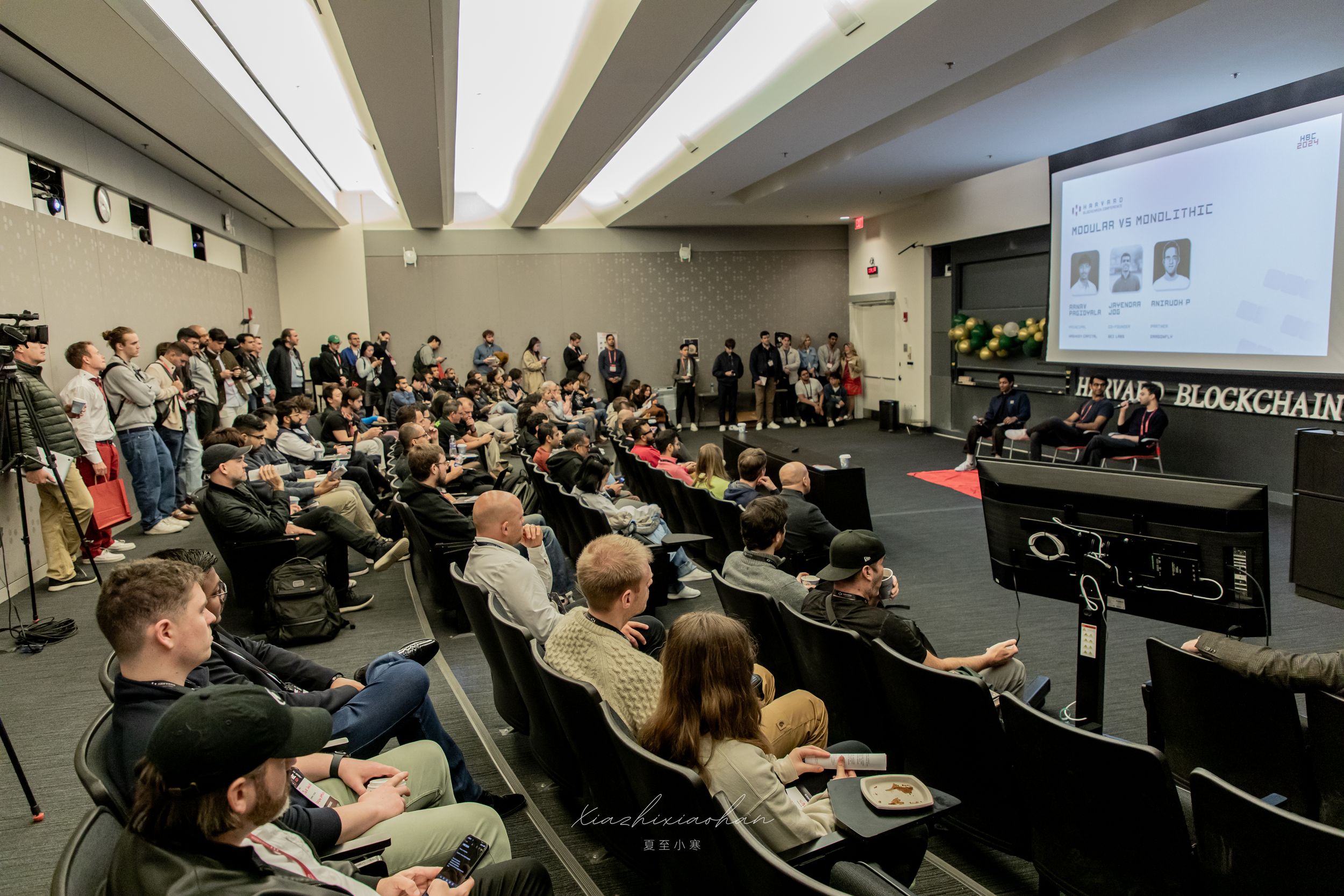Corporate presentation in darkened auditorium with projection screen and seated audience.
