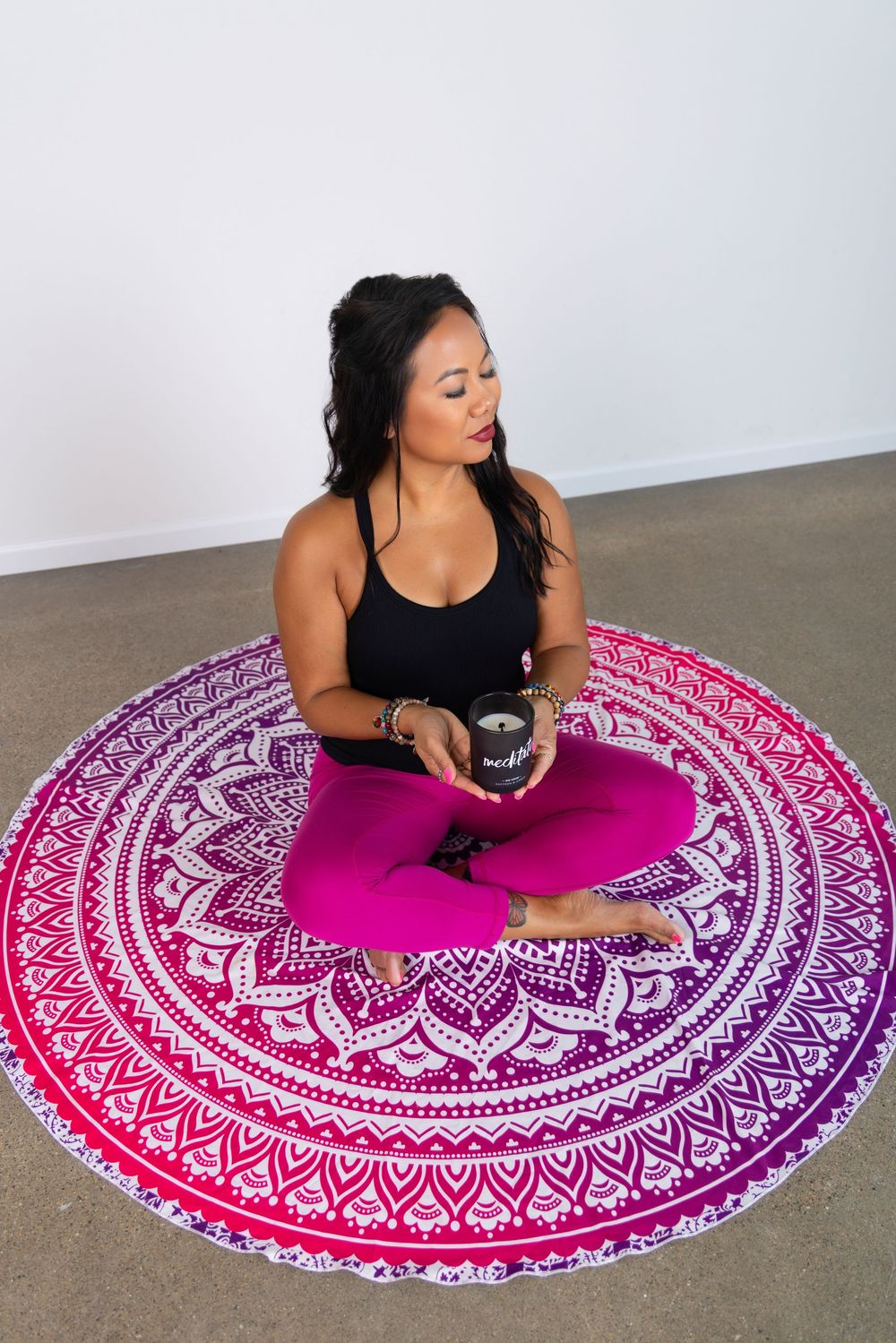 Business branding image of a life coach sitting on a colorful rug and holding a candle to signify meditation